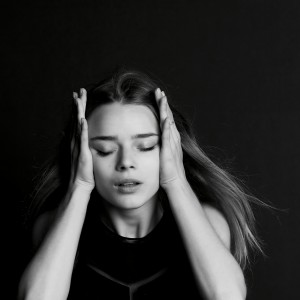 young girl holding her head in her hands against black background