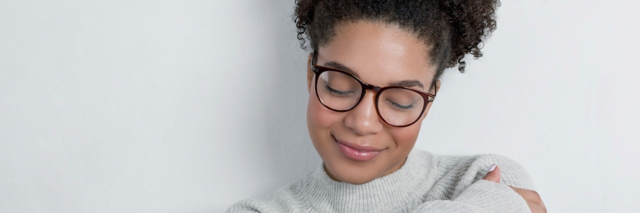 Vestibular Migraines and Laughing Through My Pain Women wearing glasses with eyes closed, smiling and arms crossed