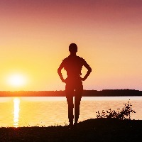 silhouette of woman standing next to lake at sunset