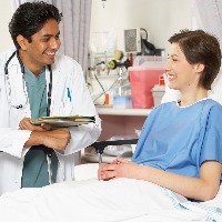 female patient laying in hospital bed and smiling and talking with male doctor