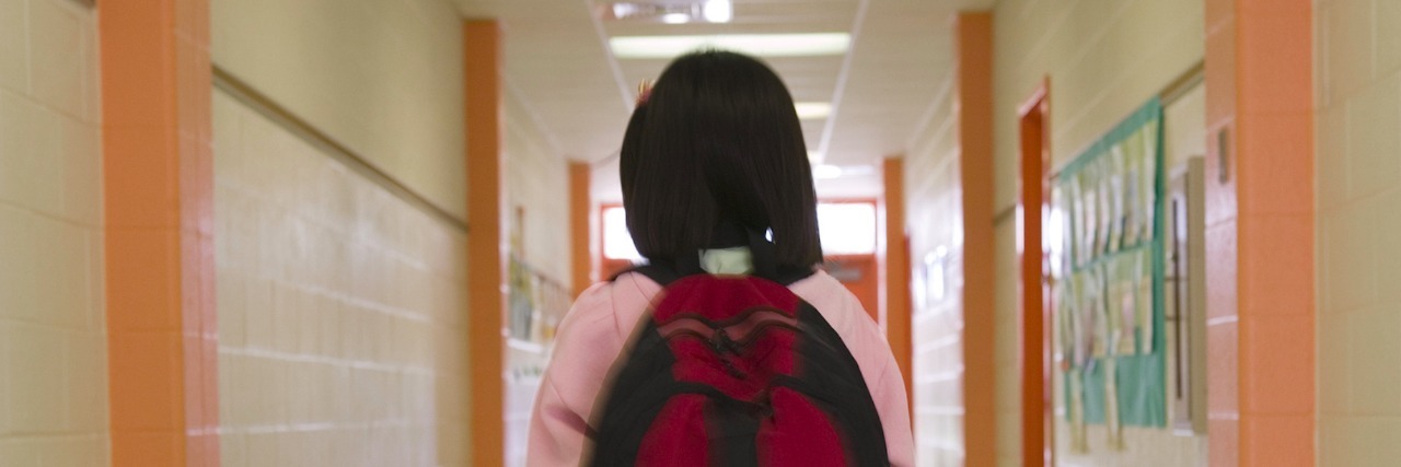 Student wearing backpack, walking down hallway at school