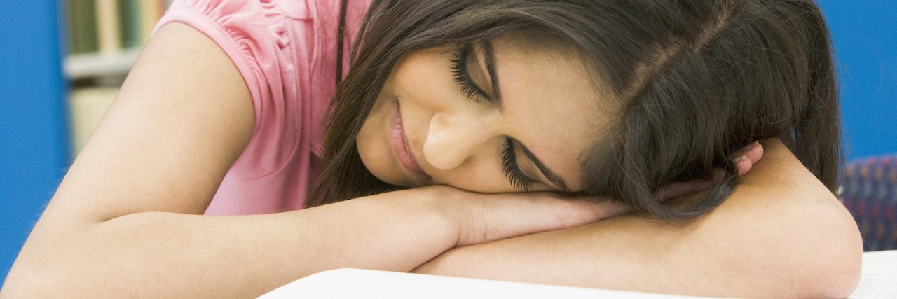 Why Mental and Physical Illnesses Make People So Tired a woman sleeping at her desk, her head on her book