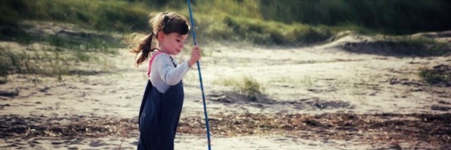 Girl walking on grassy beach, holding a net