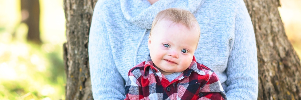 How My Child With Down Syndrome Changed My Perspective on Diversity baby sitting in mom's lap on the grass in front of a tree