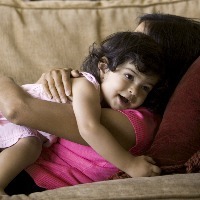 lifestyle shot of a mother as she lays on the couch and lovingly hugs her toddler daughter