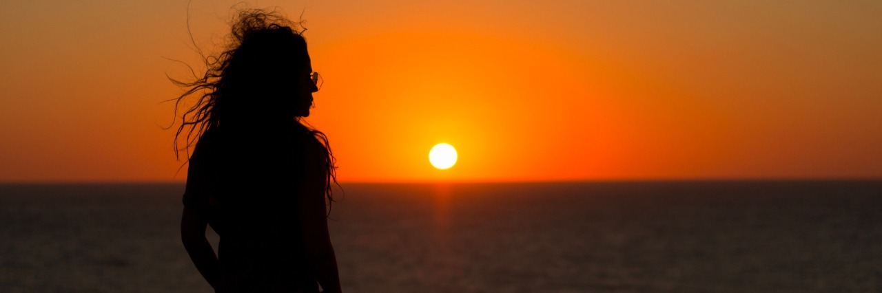 woman in silhouette looking at orange sunset