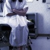 a female patient in a hospital gown sits in an exam room and waits