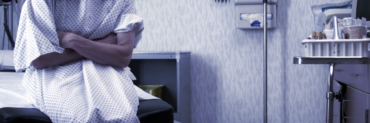 How to Deal With Anxiety From a New Diagnosis a female patient in a hospital gown sits in an exam room and waits