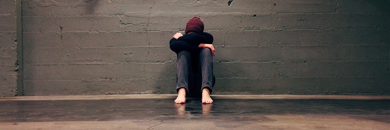 a person sitting alone in a hallway with their knees pulled to their chest and head down