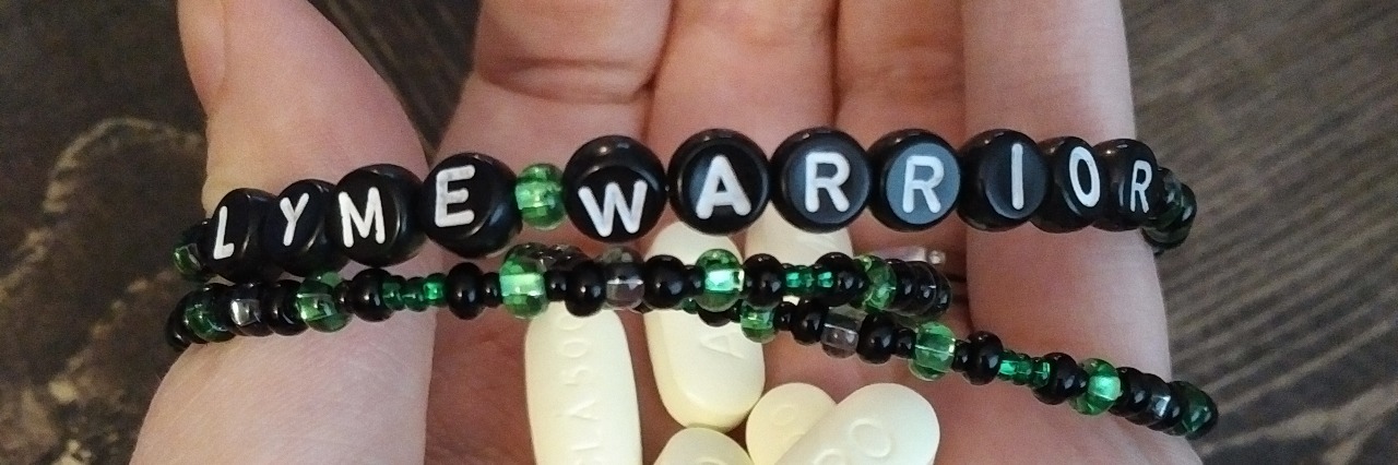 hand with bracelet saying lyme warrior wrapped around fingers