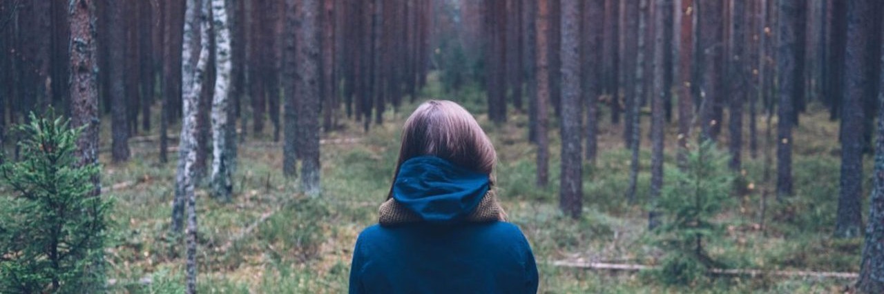 Lessons Learned After Flare-Up of Illness as a Nurse woman wearing blue jacket and facing a forest