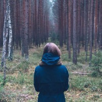 woman wearing blue jacket and facing a forest