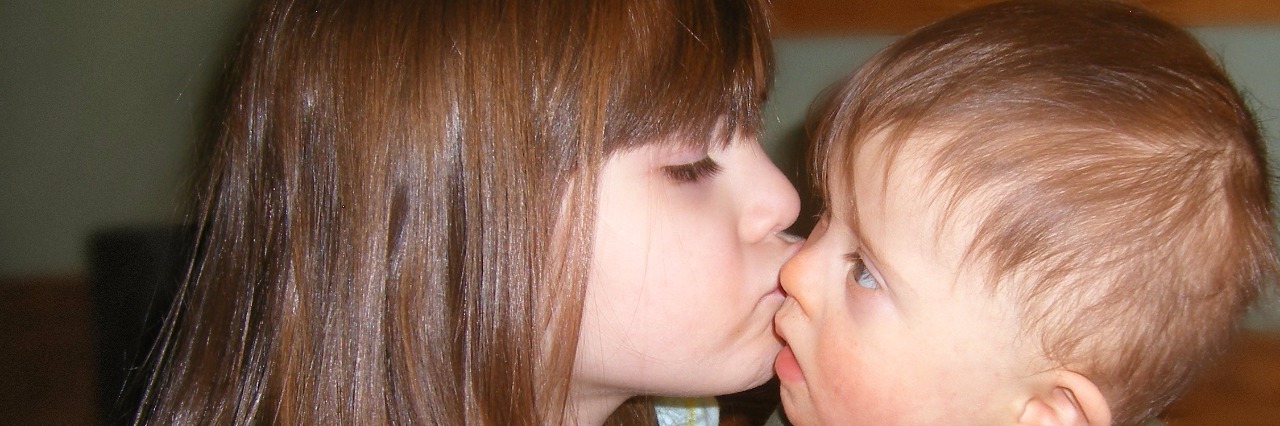 Little girl kissing a baby boy with Down syndrome