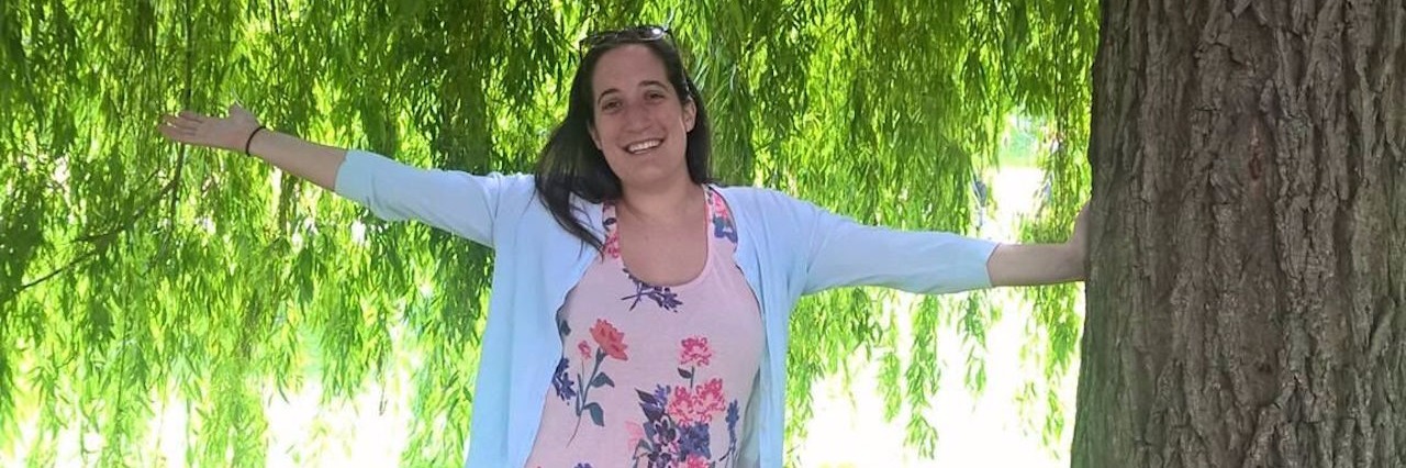 Body Image and Weight Loss, Gain With Crohn's Disease young woman standing next to a tree with her arms out