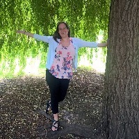 young woman standing next to a tree with her arms out