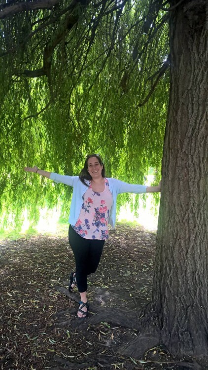 young woman standing next to a tree with her arms out