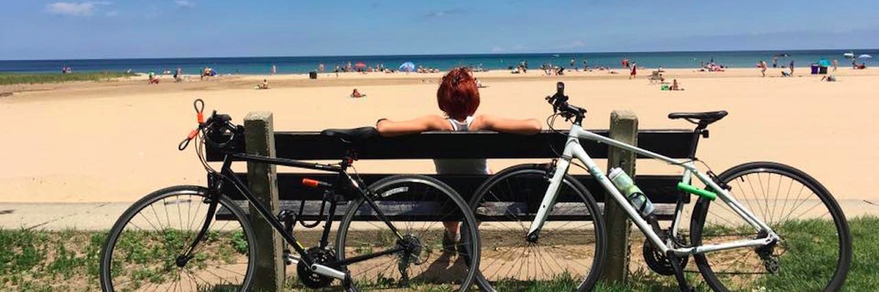 Poem About Wishing I Felt 'Normal' in Eating Disorder Recovery woman sitting on a bench looking at the beach with bikes behind her.