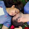 A young man and woman in-love, laying on the grass.