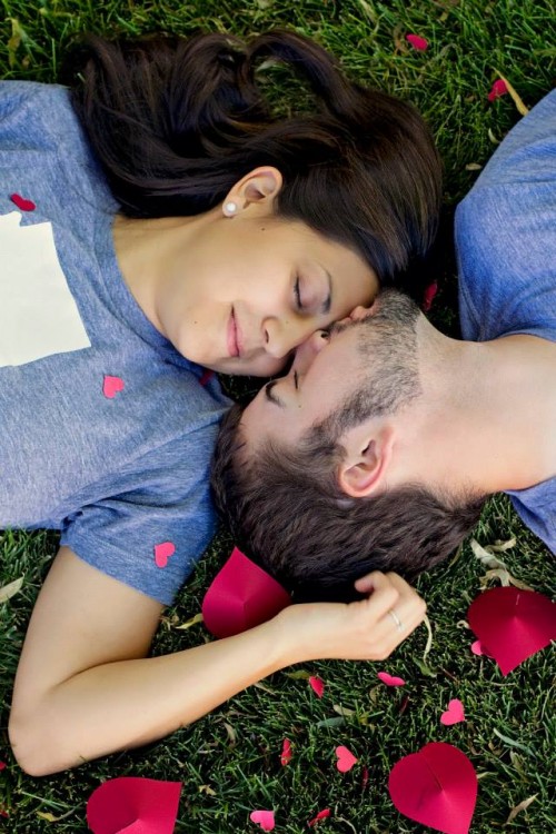 A young man and woman in-love, laying on the grass.