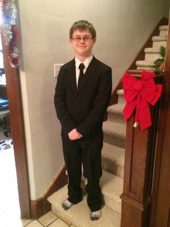 boy with down syndrome wearing a suit and standing at bottom of stairs