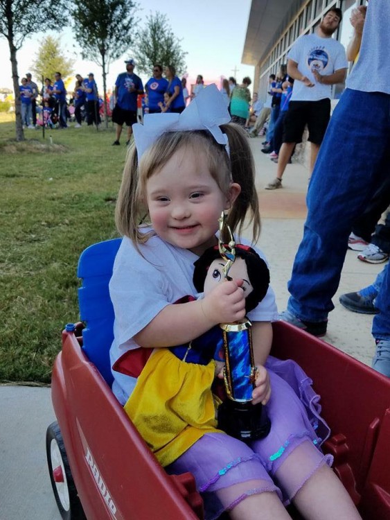 girl with down syndrome sitting in wagon holding doll