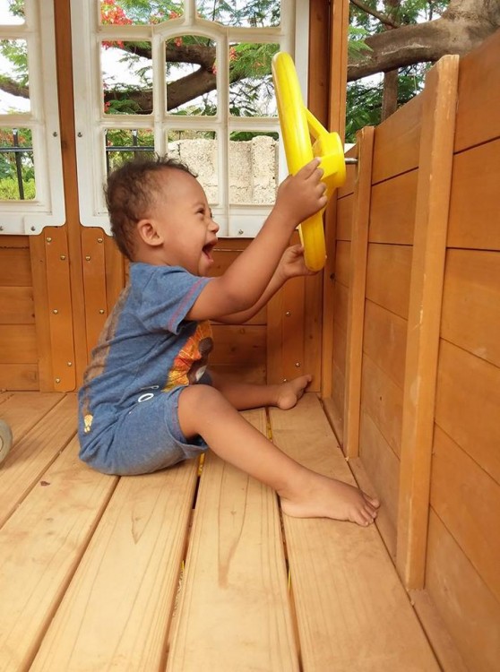 Little boy with Down syndrome playing with a yellow pirate wheel in a playset