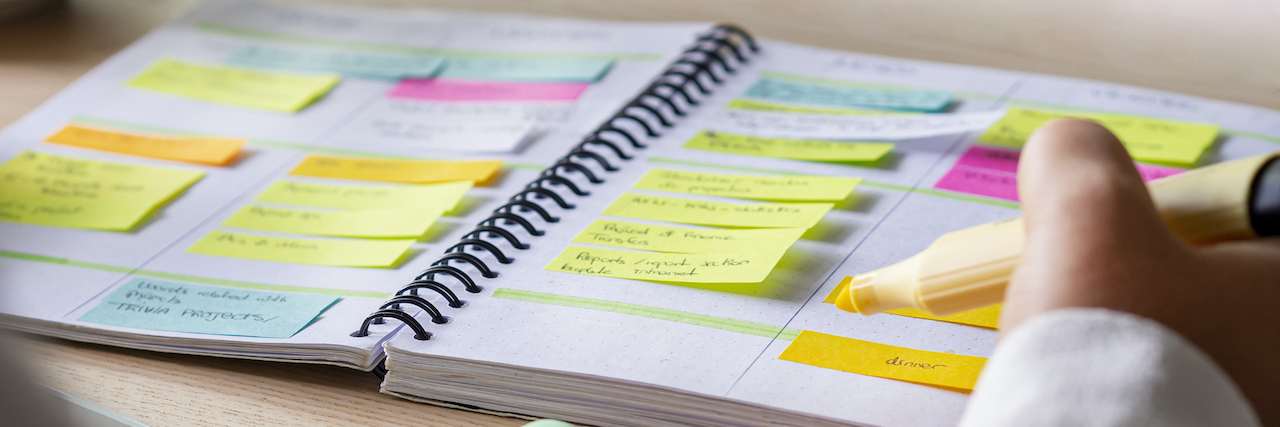 Close-up of hand holding highlighter by planner with color-coding sticky notes