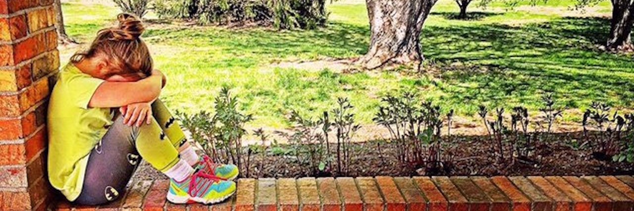 Inspirational Playlist for Bad Days With Chronic Illness young girl sitting on a brick ledge with her head between her knees and trees in the background