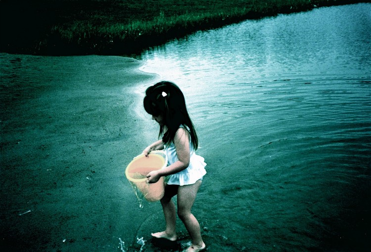young girl holding a bucket and standing in shallow water