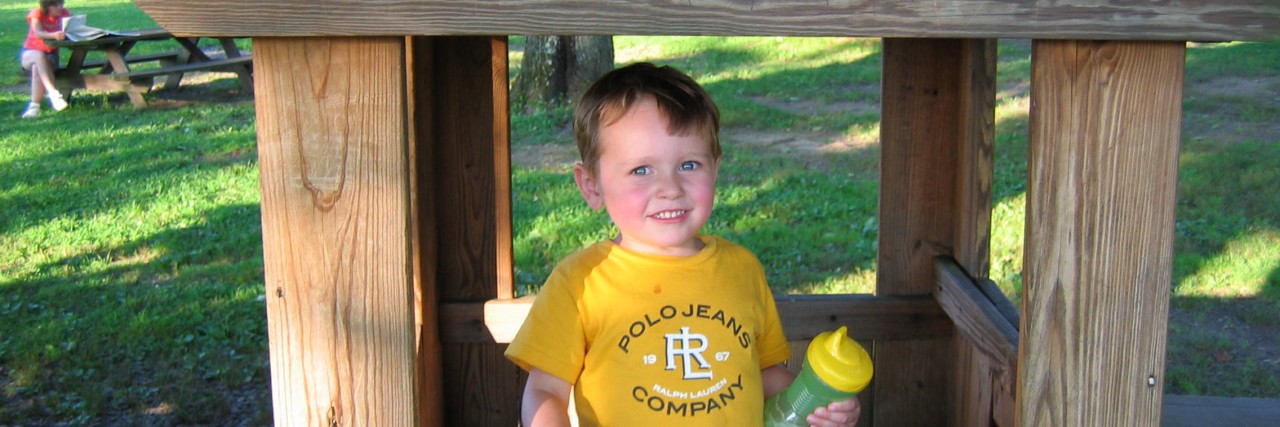 What I Wish for My Son on the Autism Spectrum Boy wearing yellow shirt and holding a sippy cup with a matching yellow top playing inside a wooden play structure.