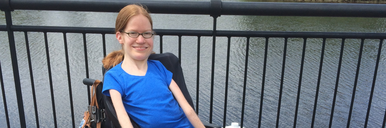 Changing Society's Perceptions About Life With a Disability Laura Robb, young woman in a blue power wheelchair sitting outdoors near a lake..