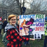 woman holding a sign that says i am not free while any woman is unfree