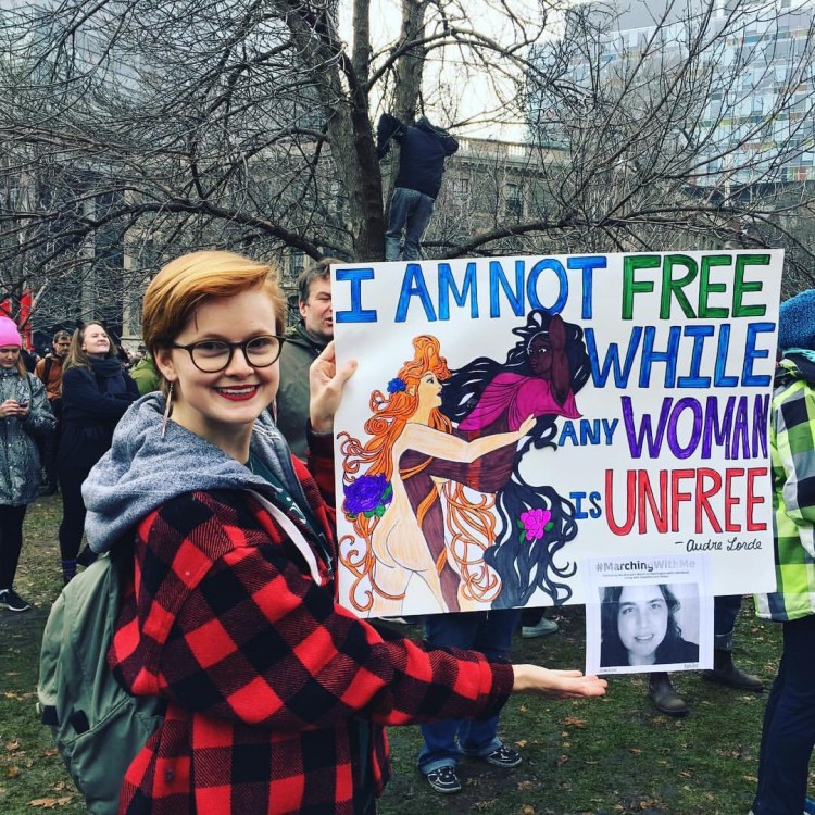 woman holding a sign that says i am not free while any woman is unfree