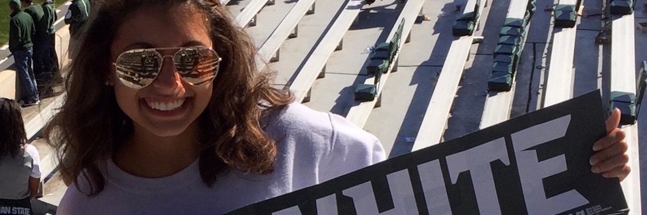 What the 'College Experience' Is Like With Gastroparesis college girl holding a banner that reads 'go white' and standing in the bleachers at a football game