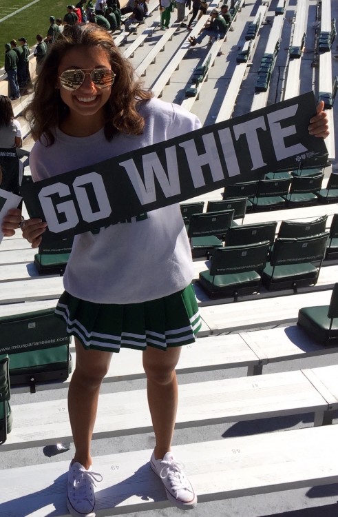 college girl holding a banner that reads 'go white' and standing in the bleachers at a football game