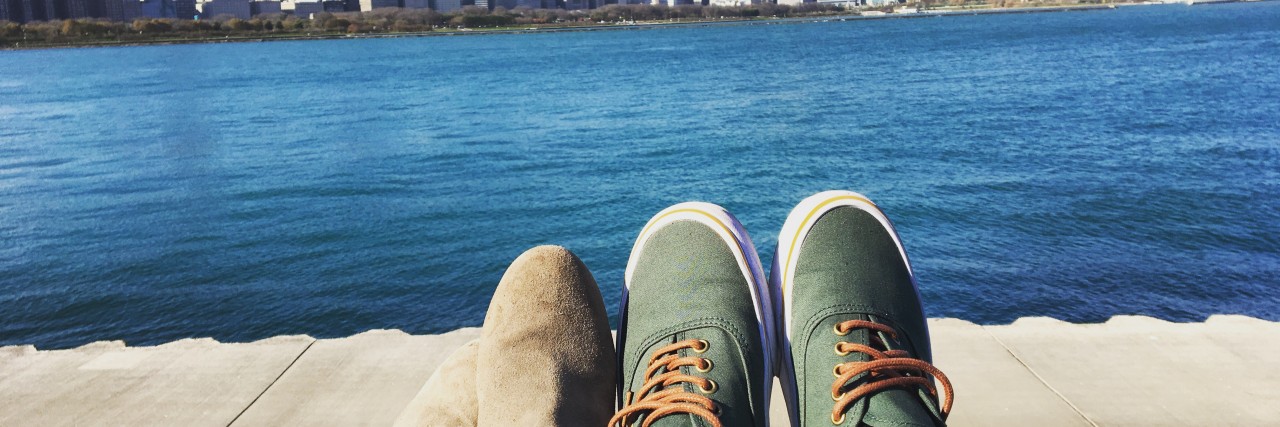 The Challenges of Dating When You're Chronically Ill A man and woman's feet, facing a body of water and a city skyscraper.