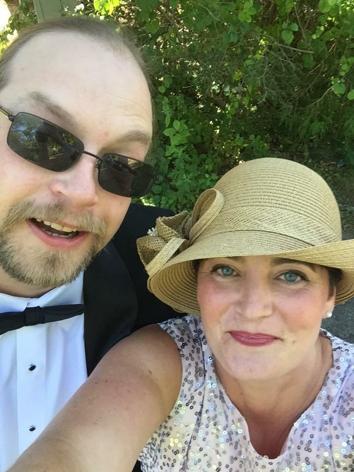 Man wearing tuxedo and sunglasses next to woman wearing hat