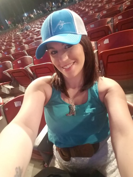 Woman wearing a baseball hat, waiting for a concert to begin.