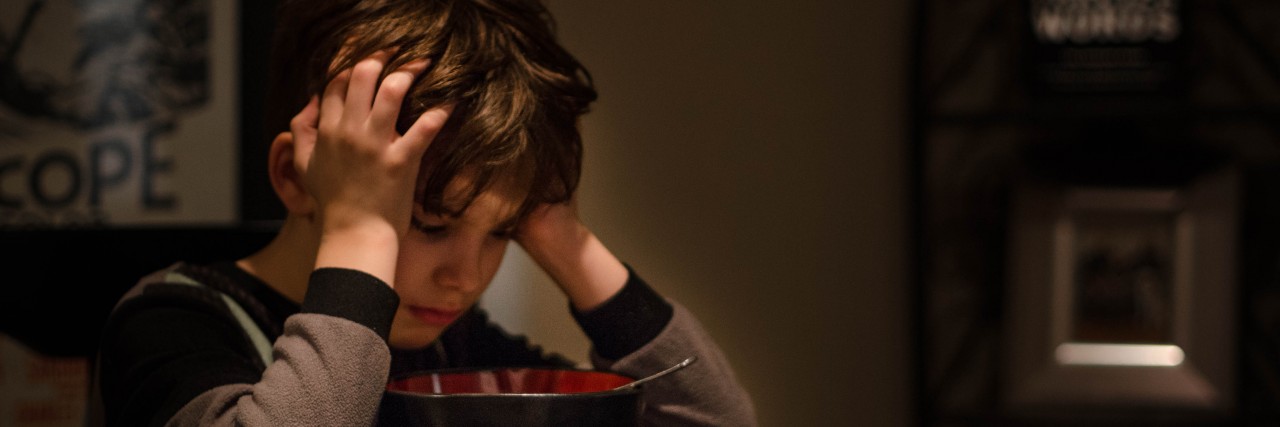 When My Son Told Me Going to School All Day Is Exhausting Picture is a boy sitting at a kitchen table staring into his cereal bowl.
