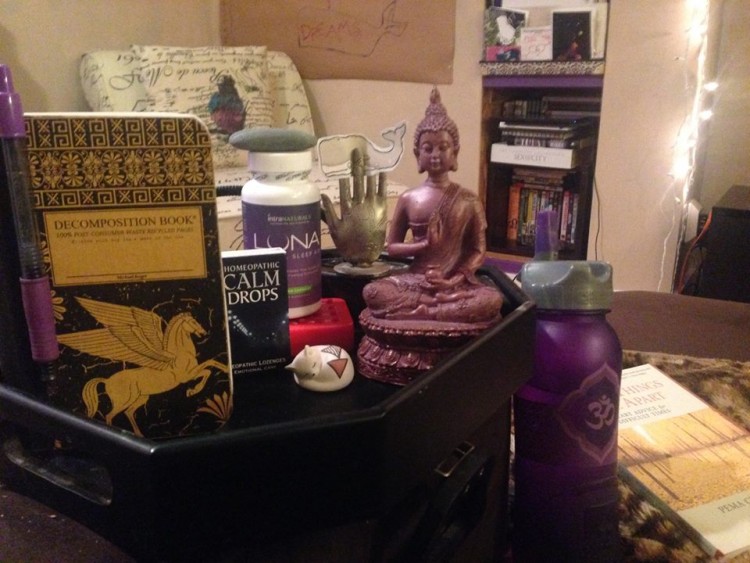 Nightstand with a purple buddha statue, calm drops and a notebook.