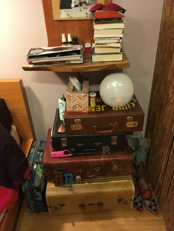 Nightstand made of suitcases with a bunch of books on top and a spherical alarm clock.