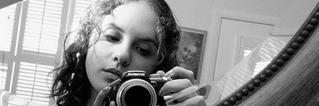 black and white image of woman being reflected in mirror holding her camera