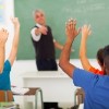 high school students with hands up in classroom with teacher pointing to student