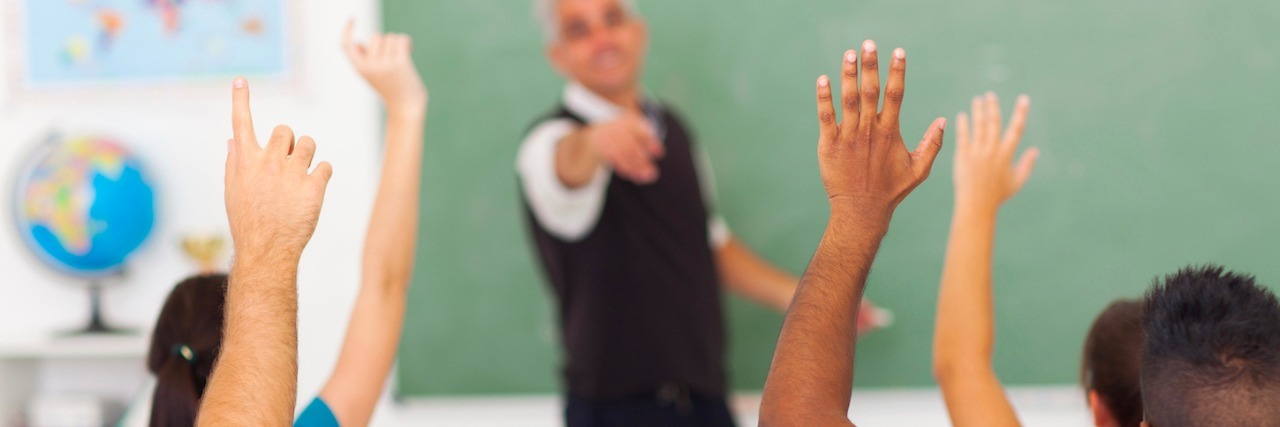Letter to the Teacher Who Gave Me Confidence to Stutter high school students with hands up in classroom with teacher pointing to student
