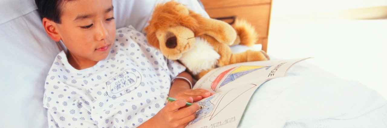 How Play Can Help a Child Cope With Stress at the Hospital Boy lying in hospital bed with toy animal, drawing in book