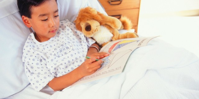 Boy lying in hospital bed with toy animal, drawing in book