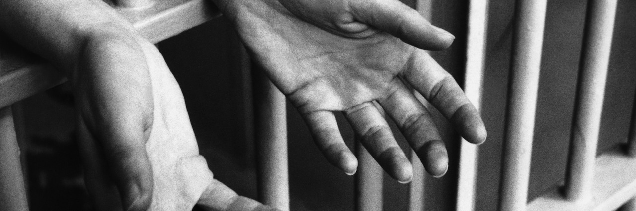 I Was Detained Under S136 of the Mental Health Act While Suicidal hands in a jail cell