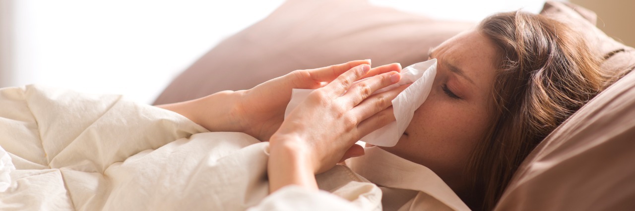 Dealing with Seasonal Sickness as a Person with Ehlers Danlos Syndrome Young sick woman blowing her nose while in bed