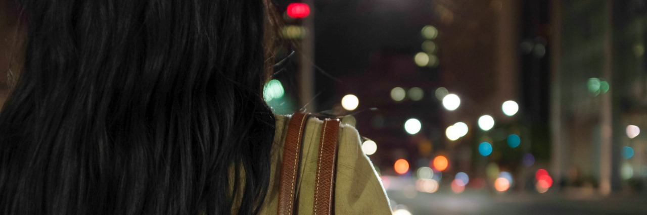 Woman standing at a street intersection at night with out of focus lights