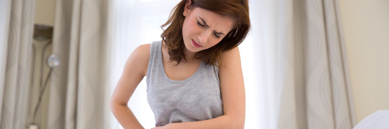 I May Look Fine, But My Lyme Disease Is Real Young woman sitting on the bed with pain in stomach